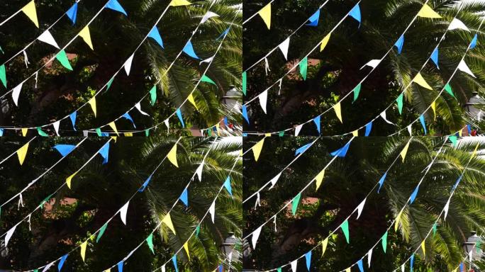 五彩三角形小旗庆祝派对迎风吹拂棕榈树。