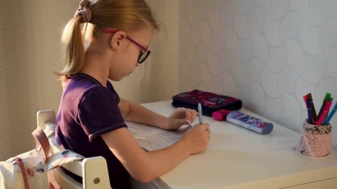 戴眼镜学习写作的小学生坐在桌子旁做作业