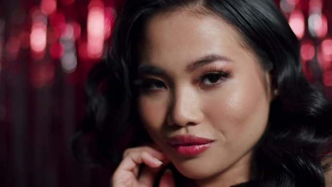 迷人魅力的亚洲女性，性感的外表在红色闪亮的背景下对着相机摆姿势。