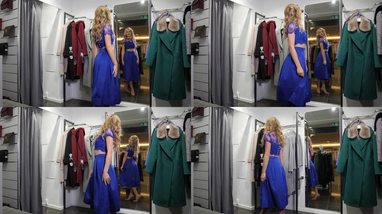 漂亮的金发女孩在时尚精品店购物，看着镜子里的新衣服