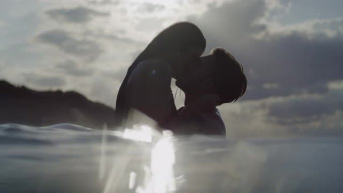 浪漫的异性恋夫妇在日落时一起在海里游泳。在水中接吻和玩耍