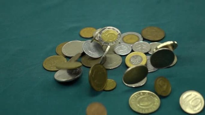 各种硬币落在一堆硬币旁边的绿色表面上，慢动作