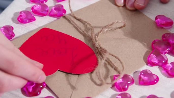 女性的手装饰着一个纸信封和一颗红色的心形纸，上面写着我爱你，特写镜头。情人节礼品包装。情人节的问候