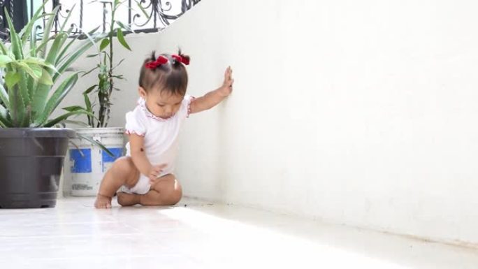 拉丁婴儿玩泥土，站起来。小女孩在房子的阳台上学习走路。