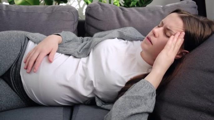不幸疲倦的年轻孕妇患有头痛或消极的想法，担心不良的产前筛查结果，躺在家里的沙发上。对分娩概念感到恐惧