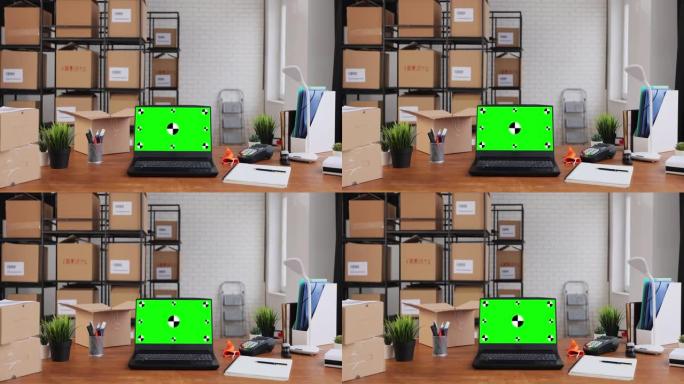 带有绿色屏幕chromakey显示模型的笔记本电脑站在仓库的桌面上。背景中的纸板箱。