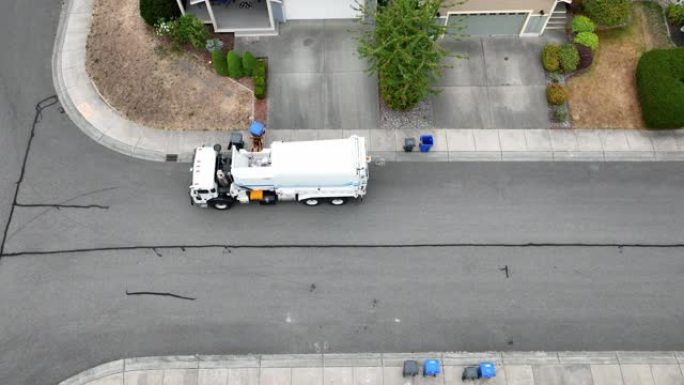 一辆垃圾设施卡车从郊区家庭捡起一堆回收物的鸟瞰图。