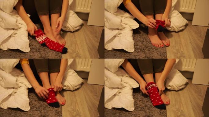赤脚女人坐在寒冷房间的地板上，光线昏暗。裹上白色保暖毯，穿上红色图案的袜子。室内低温。没有暖气，冬天