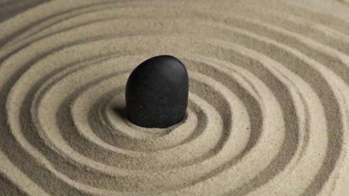 黑石在沙子螺旋中心的旋转。沙子中的图案特写