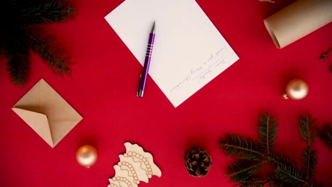 给圣诞老人的祝贺信手写在一张红色背景的白纸上，靠近信封，钢笔，冷杉树枝和金色的圣诞节球。