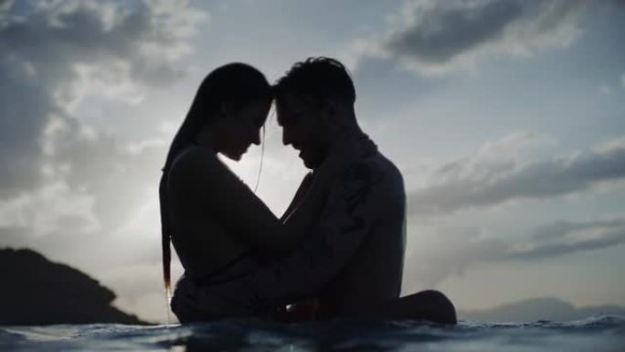 暑假浪漫的异性恋夫妇。在美丽的金色日落时在海里游泳。亲吻和拥抱