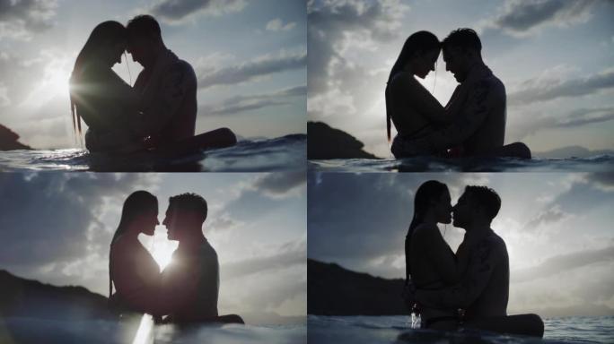 暑假浪漫的异性恋夫妇。在美丽的金色日落时在海里游泳。亲吻和拥抱