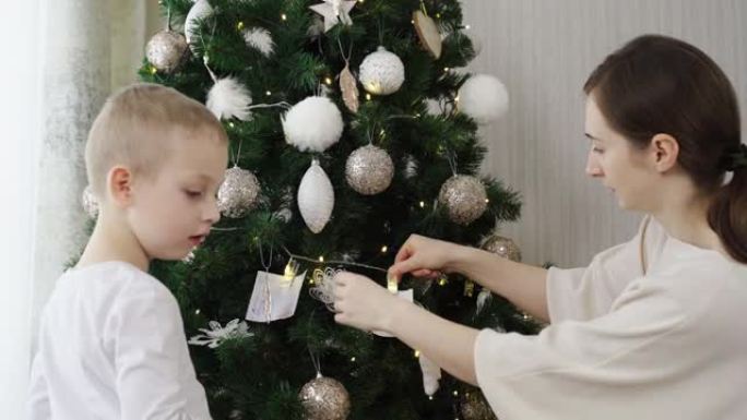 一个小男孩和母亲在圣诞树上挂着一张写着愿望的纸条。