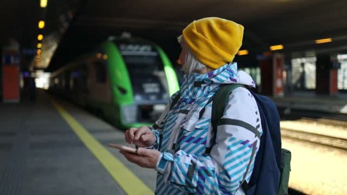 在火车站使用智能手机旅行50多岁的妇女。高级高加索旅行者在终端或火车站用手机应用程序检查登机时间。