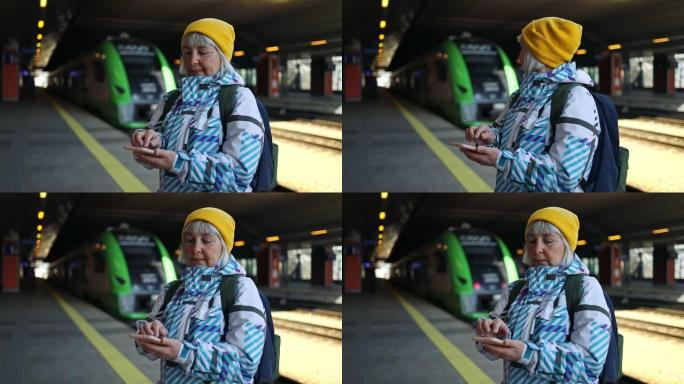 在火车站使用智能手机旅行50多岁的妇女。高级高加索旅行者在终端或火车站用手机应用程序检查登机时间。