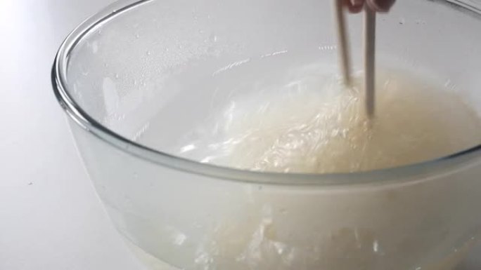 用筷子在热水中搅拌和冲洗玻璃纸面条 (funchose，fansi)
