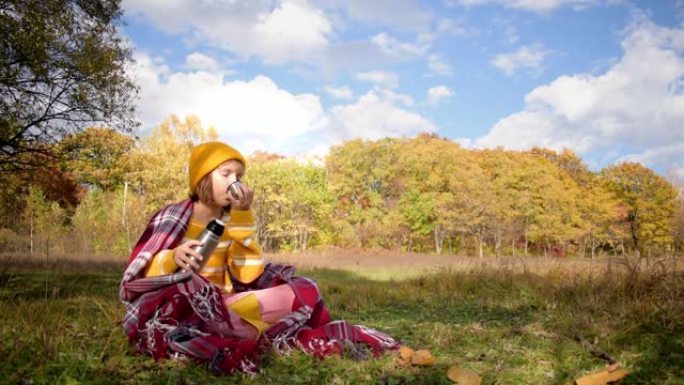 特写女孩徒步旅行者在阳光明媚的秋日喝热茶，在秋天的森林里放松。保健，真实性，平衡感和镇定感。慢动作视