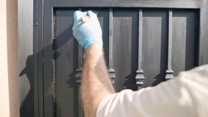 戴着手套的工人用画笔和黑色着色翻新了金属门表面，在建筑工地用钢表面工作。专业杂工修复旧腐蚀闸门，老化