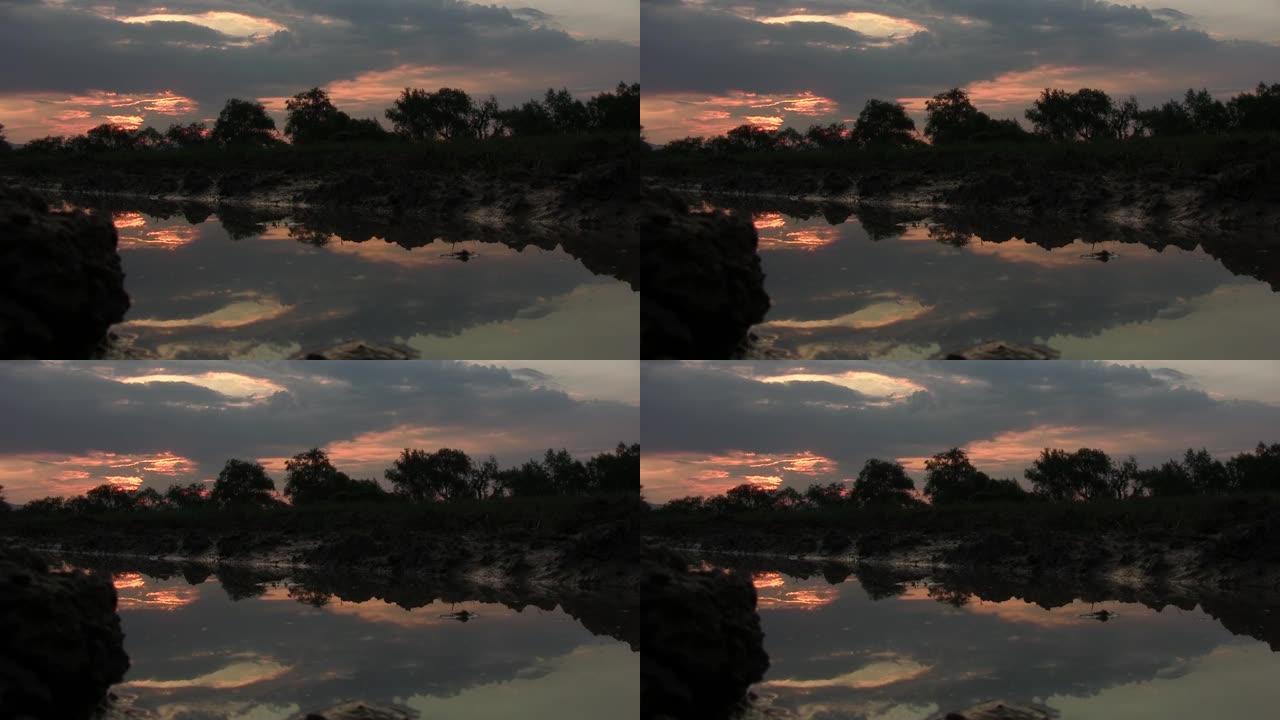 日落时在道路边缘拍摄的图像。天空阴云密布，太阳的光芒泛红。地球是湿的，这是一个大池塘