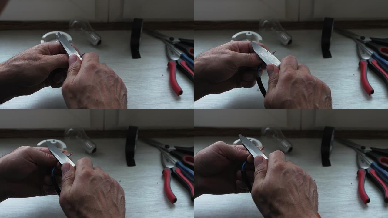 电工用刀剥去电线。把电连接到电线上。一个人削尖电线连接灯