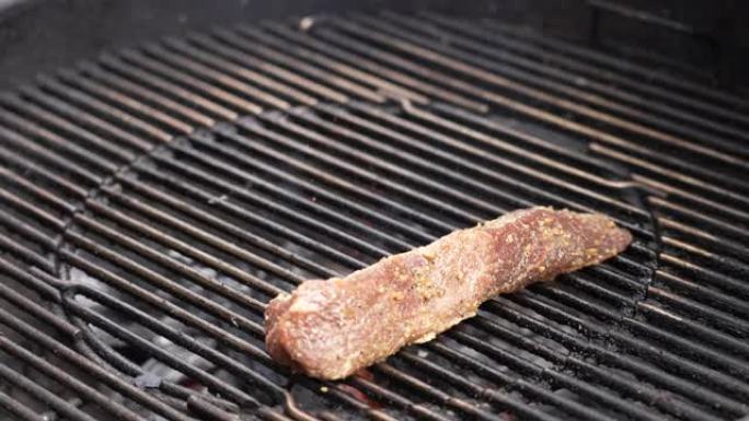 将腌制的三尖牛肉片放在后院的热煤烤架上-慢动作地嘶嘶作响并吸烟