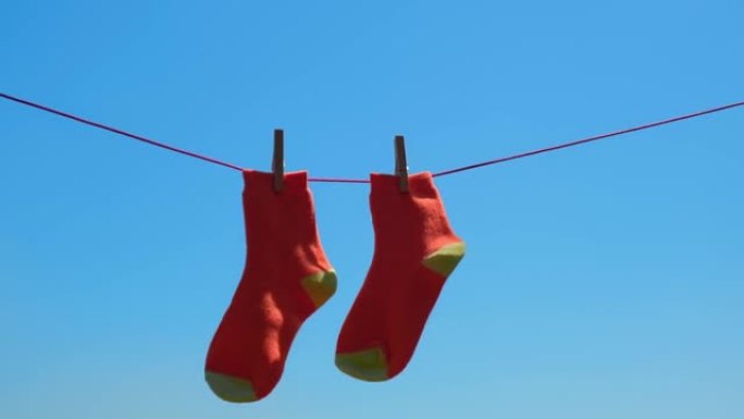 一双橙色袜子在绳子上洗涤后特写干燥，在蓝天下随风摇曳。