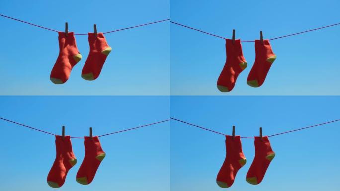 一双橙色袜子在绳子上洗涤后特写干燥，在蓝天下随风摇曳。