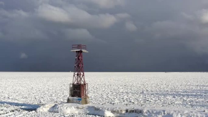 从冰雪覆盖的密歇根湖飞向码头，码头的末端是钢制的红色塔楼结构，上方是多云的蓝色和灰色天空。