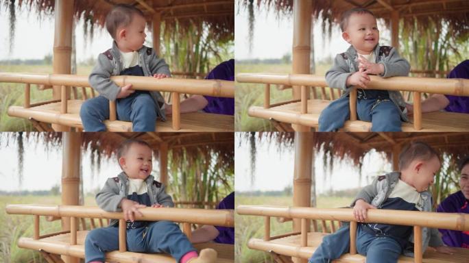 可爱的亚洲小男孩坐着和他的母亲在户外开心地笑着玩耍的真实照片。为人父母，母亲节概念。