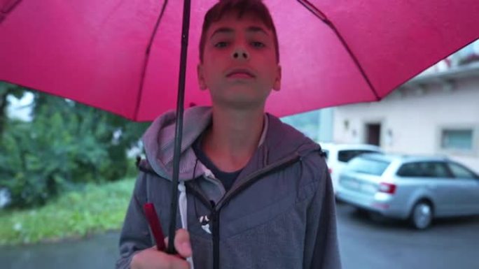一个小男孩在下雨时拿着红伞走在外面。下雨天，青春期的孩子在户外散步