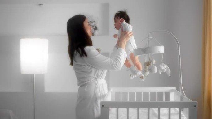 妈妈抱起一个躺在婴儿床里的新生婴儿。白色儿童房。