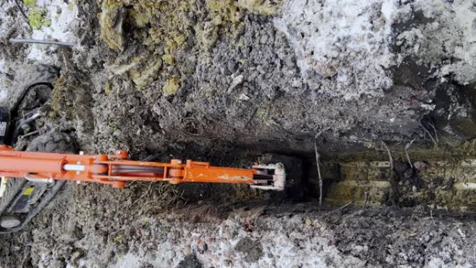 在冬季，挖掘机的铲斗从地面上取土的垂直镜头。