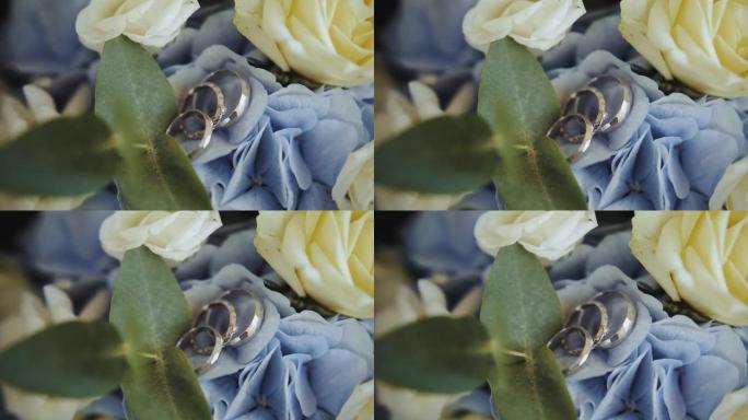 结婚戒指躺在新娘花束的花瓣上，蓝色绣球花和白玫瑰，婚礼配件慢动作