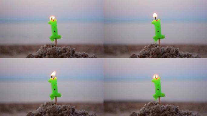 蜡烛一号在棍子上插入沙子和燃烧。模糊海浪背景下的沙子点燃蜡烛。模糊的蓝色棕色背景上的绿色燃烧蜡烛。生