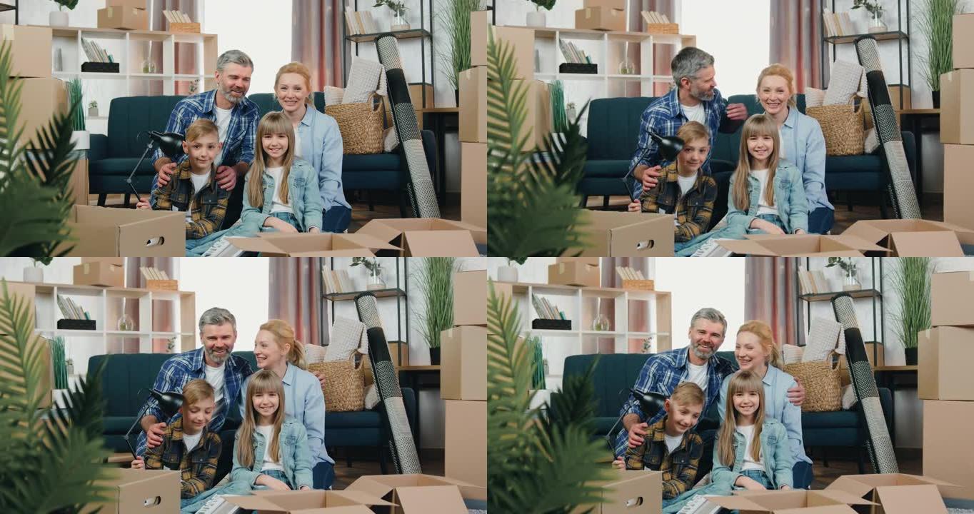 可爱的快乐快乐友好家庭的特写肖像，搬入新公寓后，他们在相机上与纸箱中的拥抱合影