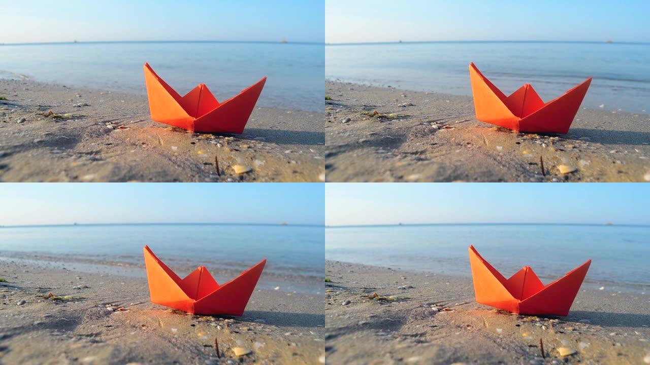 小纸橙船在海浪背景下靠近水面的沙子上特写。沙滩上的纸船夏天阳光明媚的日子。概念冒险旅行度假假期休息旅