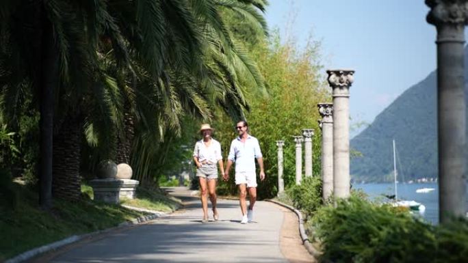 男人和女人手牵着手穿过湖边的公园，穿着休闲的夏装