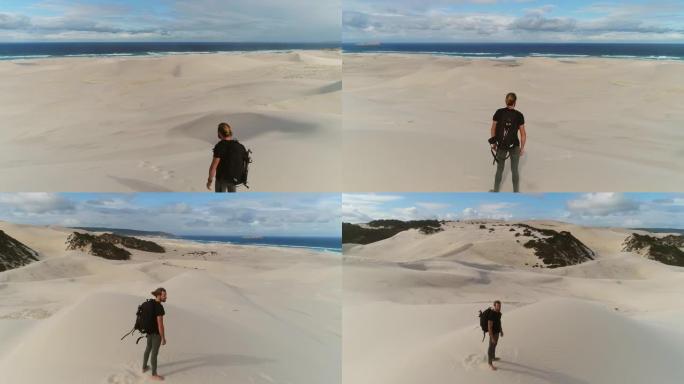 年轻人站在沙丘上的干旱沙漠场景，敬畏和沉思着大海