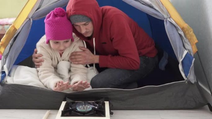 孩子和爸爸在帐篷里的煤气炉旁取暖。冬季供暖和天然气危机。由于能源危机，停止供电和集中供暖。