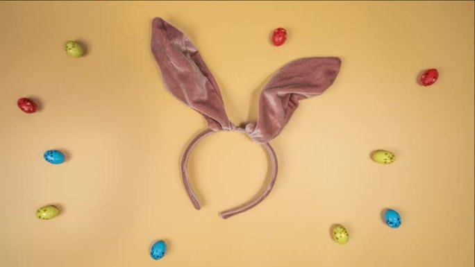 多色复活节彩蛋在橙色背景上的运动，兔子耳朵。复活节快乐。朝一个方向滚动。传统春季庆典的概念。新生活的