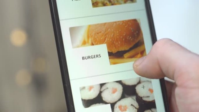 使用智能手机与应用程序交付食物在屏幕上进行在线订购的男性双手特写。