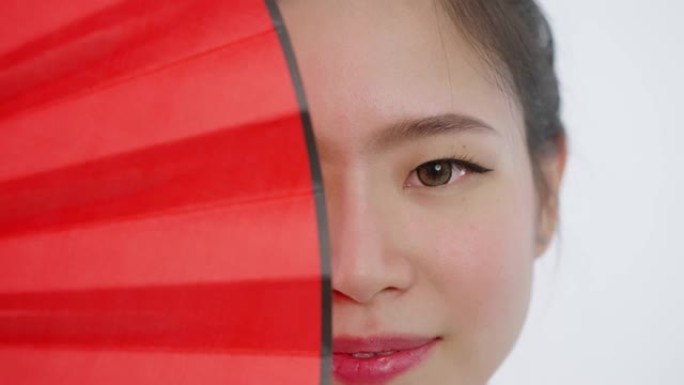 中国/亚洲美女脸部特写春节红扇遮住右半脸，看着镜头