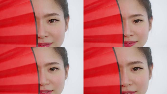 中国/亚洲美女脸部特写春节红扇遮住右半脸，看着镜头