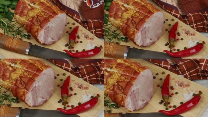 一块多汁的猪肉火腿放在木制切菜板上，旁边是一把雕刻刀、多色五香豆、红辣椒、欧芹、莳萝和罗勒。美味肉制