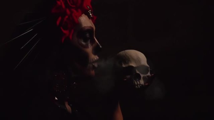 一个女人，脸上有死亡女神或卡塔琳娜风格的图案，在背景上的脸前有一个糖头骨，在头骨上吹白烟。死者的节日