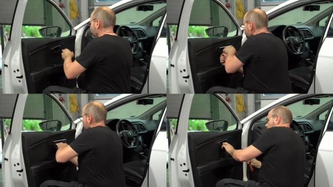 Man专业汽车修理工正在汽车修理厂通过无油漆凹痕修理方法拆卸门板来固定车门。拆卸门的过程