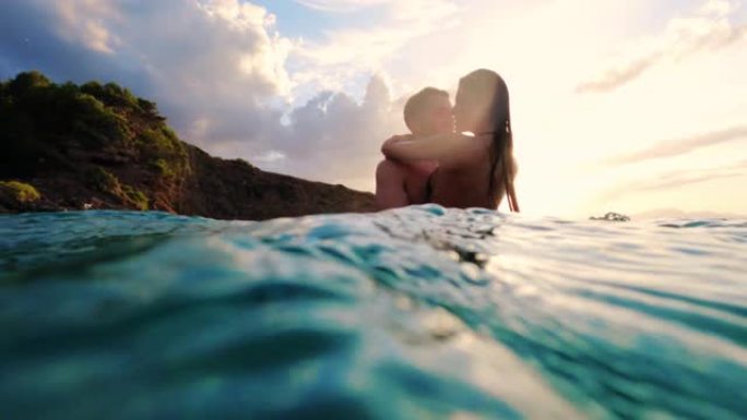 暑假浪漫的异性恋夫妇。在金色日落时拥抱在绿松石水中