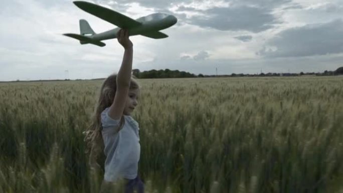可爱的小女孩手里拿着飞机玩具在麦田里奔跑，相机跟随