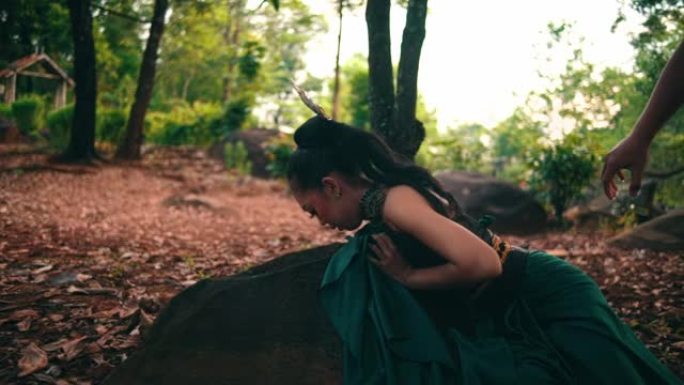 一名穿着绿色衣服和黑色长发的亚洲妇女在森林中央被她的朋友欺负后在岩石上哭泣