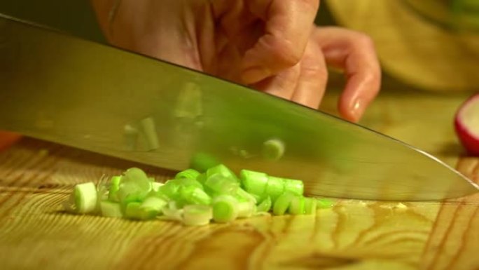用刀在木板上切厨房里的葱。特写。